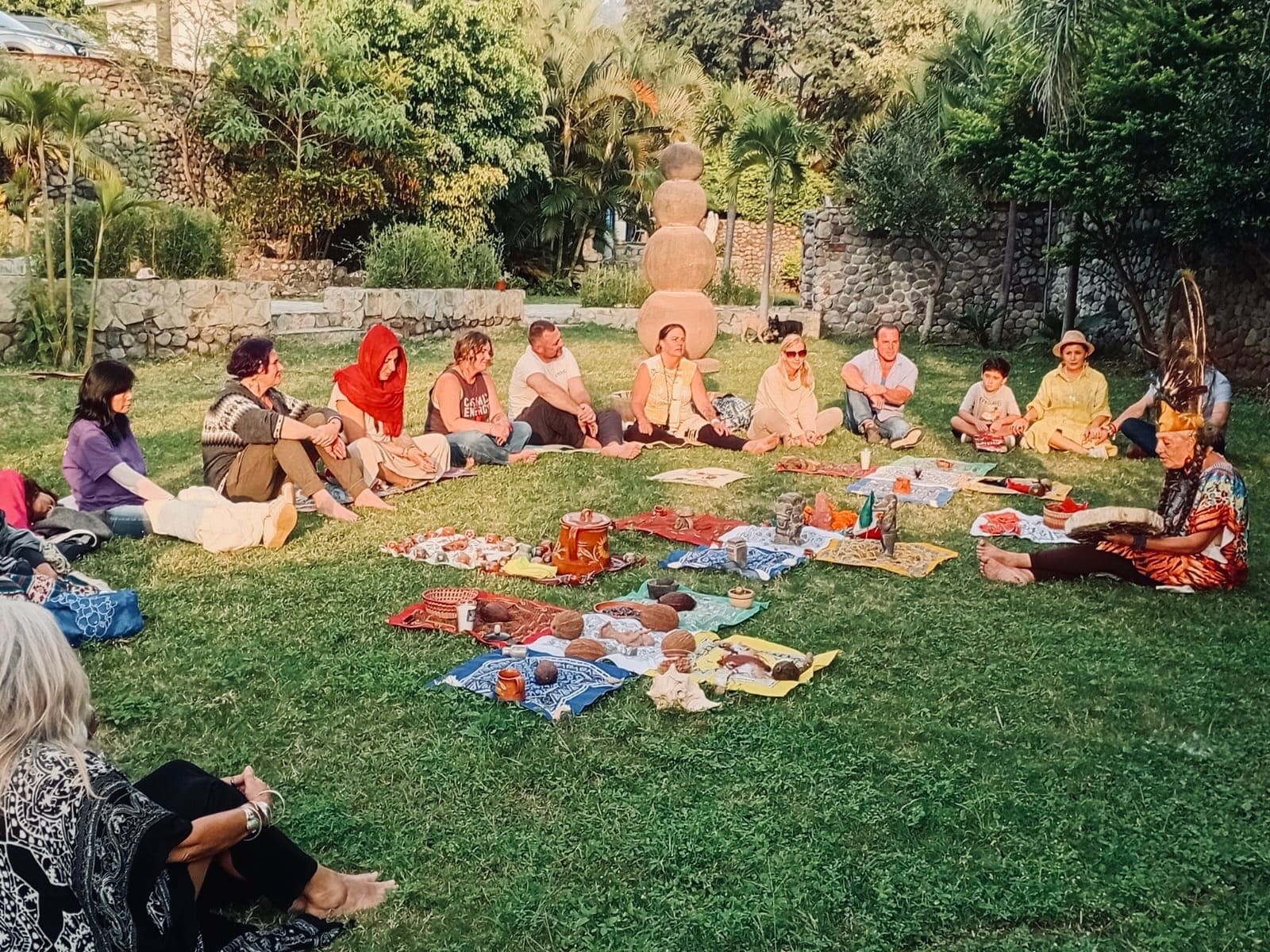 A group seated in a circle on the grass in a sunlit garden